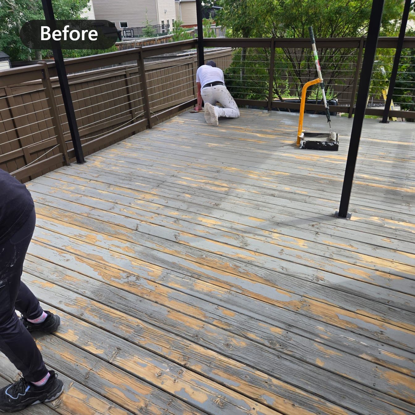 Raised deck with bare weathered boards before refinishing, painter at work