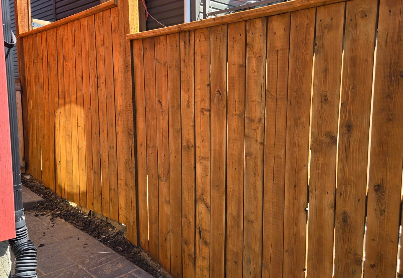 The same cedar fence after staining, rich warm orange-brown finish